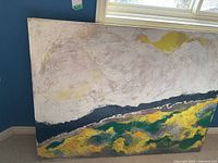 Full view of the abstract landscape oil painting leaning against a wall showing textured brush strokes and color blocks in cream, yellow, dark blue, and green tones.