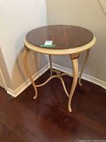 Round ornate wooden table with cream colored legs and dark wood top, shown from an angled front view.