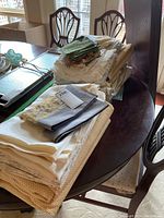 Wide view of multiple folded table linens stacked on a round dining table showing varied fabrics and textures including napkins and cloths.
