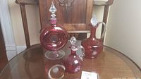 Three cranberry glass handblown decanters on table, showcasing overall lot