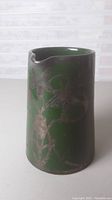 Angle showing front and side of green ceramic pitcher with metal floral overlay.