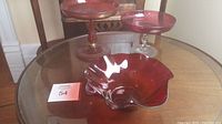 Photo of three cranberry glass pieces on round wooden table: two footed dishes and one open bowl with wavy rim