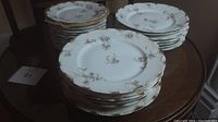 Stacks of 14 larger and 12 smaller floral porcelain Limoges plates on a wooden table.
