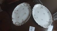 Two large porcelain platters featuring floral patterns and ornate edges on a wooden table