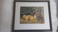 Framed watercolour painting showing entire scene of pumpkins on hay beside red wagon wheel.