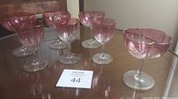 Full set of eight pink crystal glasses on a wooden table, showing two distinct sizes and decoration.