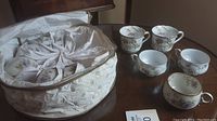 Photo of 11 porcelain teacups on a table with white fabric for protection showing floral designs and gold rims.