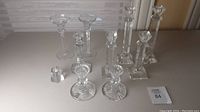 Wide view of the collection of nine vintage glass candle sticks arranged on a white surface, showing different sizes and designs.