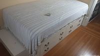Side view of wooden bed base with mattress; four drawers visible