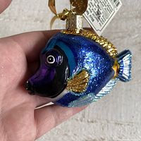 Front close-up showing detailed painting and glitter on glass ornament of blue tang fish with hanging tag.