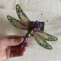 Front view of colorful glass and plastic dragonfly ornament held in hand showing wing and body details.
