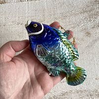 Front side of blue glass fish ornament showing scale texture, white head accents, and attached hanging loop with gold chain