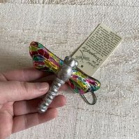 Front view showing colorful stained glass wings, silver segmented body, and attached tag.