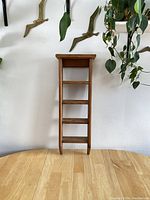 Front view of the rectangular hanging wood wall shelf with four shelves against a white wall, shown on wooden table.