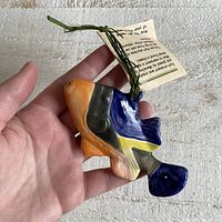 Photo of hand holding colorful pottery fish ornament showing front and attached tag.