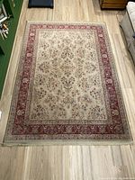 Full view of the rectangular red and tan area rug spread out on light wood flooring with visible fringe at the bottom edge.
