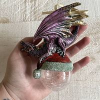 Front view showing purple dragon perched on red and green glitter base above clear glass orb.