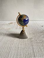 Full view of small globe on brass stand showing size and overall condition with rough cloth textured surface under item.