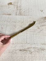 Letter opener held in hand on textured surface showing overall shape and size.