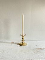 Front view of the brass candle stick holder with white candle placed in it, showing polished brass base and stem with glass frilled bib near top.