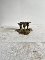 Three-quarter angle view of the brass candlestick holder on a textured white surface showing flower-shaped candle cups and leaf base.