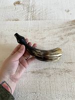 Photo showing the overall shape and size of the carved horn whistle held in hand for scale.