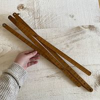 View of the pantograph arms held out spread on a light wood surface showing multiple arms connected by pivots with measurement scales.