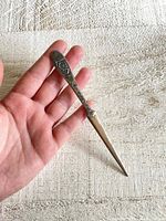 Full view of the vintage metal letter opener held in hand showing overall length and shape.