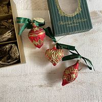 Three Waterford Nostalgic Collection ornaments displayed outside the box, showing decorative gold accents on red glass and green ribbons.