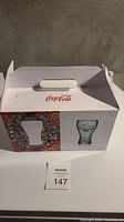 Closed white box with Coca-Cola and glass image on front with handle on top