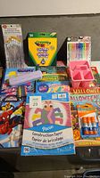 Photo showing assortment of colouring and craft supplies including coloured pencils, scrapbook paper, Halloween colouring books, glue sticks, and craft trays.
