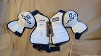 Photo showing white Jofa chest protector with lace tie and size XL tag alongside pair of matching white Jofa shoulder protectors with blue trim and logos.