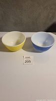 Two small Pyrex bowls displayed side by side, showing yellow and blue exteriors with white interiors.