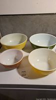 Set of 4 Pyrex mixing bowls in varying colors on a white surface