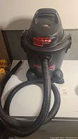 Photo showing the full Shop-Vac unit with attached hose and nozzle at its front, standing on four caster wheels