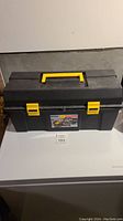 Closed view of a black plastic tool box with yellow handle and latches