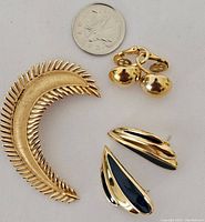 Trifari brooch, gold-tone feather shaped, with coin for scale, two pairs of earrings: gold-tone clip-ons and gold-tone with black enamel studs.