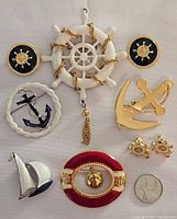 Overview of all five vintage nautical-themed brooches and two pairs of earrings arranged on white background, with a quarter coin for size reference