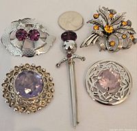 Full lot overview showing all five pins with their stones and designs visible next to quarter for size reference