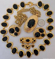 Full set of gold tone and black stone jewelry laid out with quarter for scale.