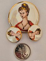Front view of hand painted brooch and earrings next to a Canadian quarter for size reference.