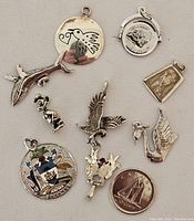 All nine silver charms displayed on light background, showing varying designs including animals, crest, coin, and symbolic shapes.