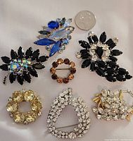 All seven vintage rhinestone brooches displayed with US quarter coin for size reference.