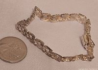Silver bracelet lying on fabric with a coin beside it for scale, shows length and clasp type