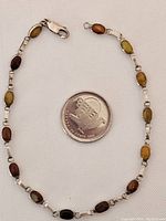 Top view of the bracelet alongside a quarter to show scale. The bracelet is composed of oval stones set in sterling silver with small linked connectors.