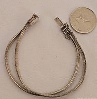 Sterling silver bracelet with clasp and 7-inch length for scale alongside a Canadian quarter coin.