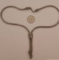 Full view of the sterling silver necklace laid out with a coin for size reference showing the toggle clasp and dual hanging strands.