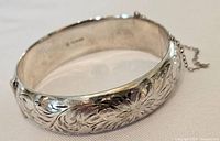 Close-up of the bangle showing floral and swirl engraving on the outside with a silver shiny finish.