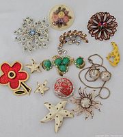 Overview of thirteen vintage jewelry pieces featuring various brooches and earrings including floral, starfish, and animal motifs