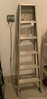 Full front view of tall aluminum step ladder leaning against wall with six steps visible.